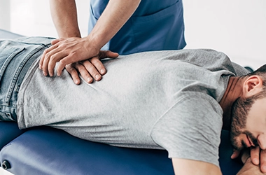 Chiropractic Doylestown PA Patient Receiving Adjustment HP Man Lying Face Down On Blue Table While Someone Adjusts Their Lower Back